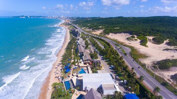 An aerial view of a coastal hotel with a beachside location, a swimming pool, and a road running parallel to the beach.