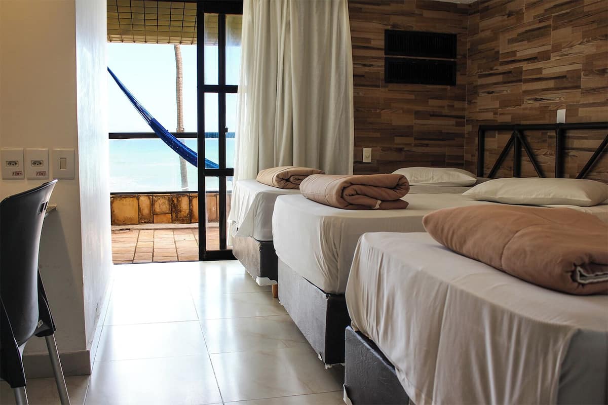 Habitación de hotel con dos camas, vista al mar a través de un ventanal grande y una hamaca afuera.
