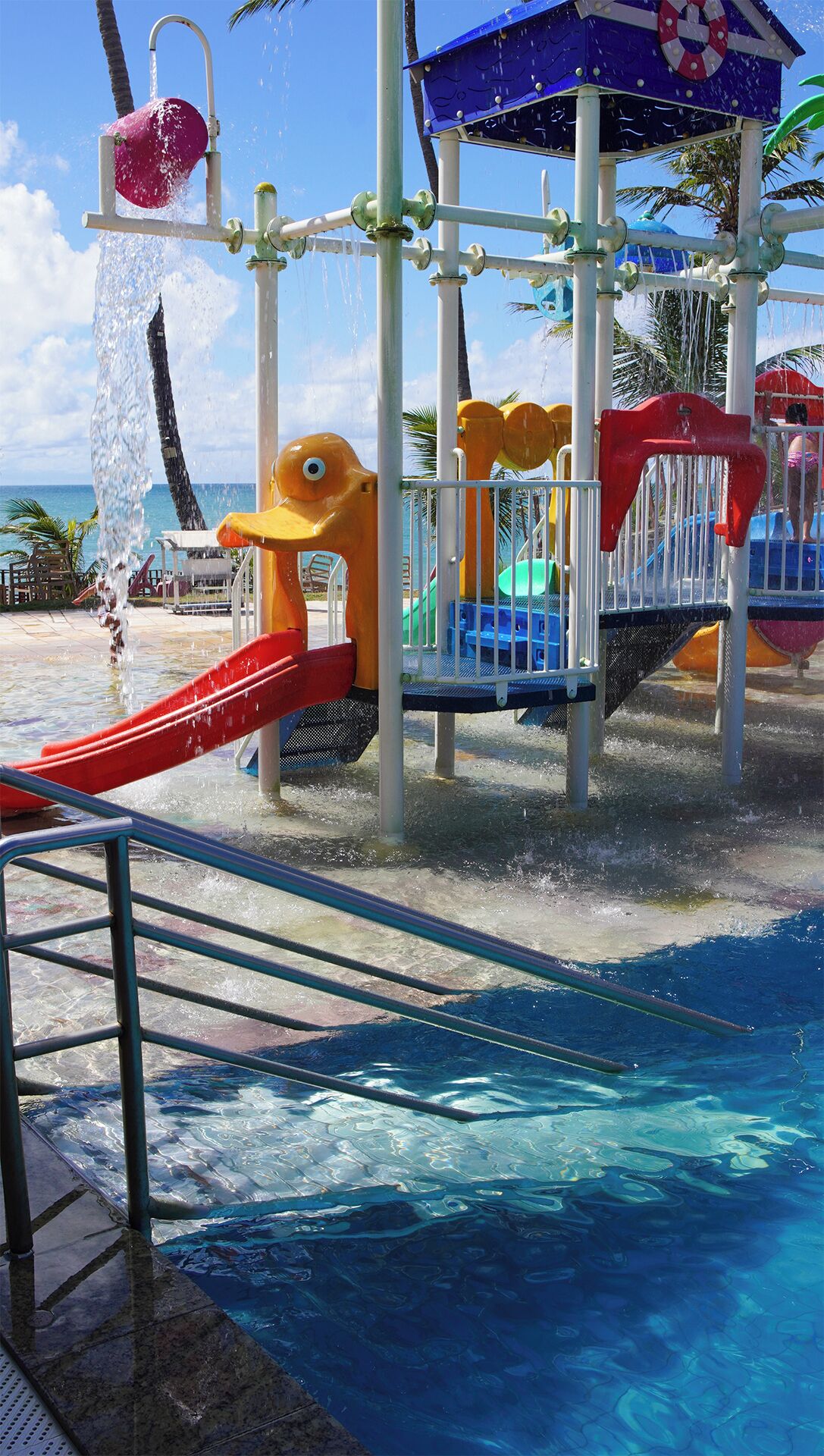 Zona de juegos acuáticos con toboganes y chorros de agua, rodeada por una piscina.