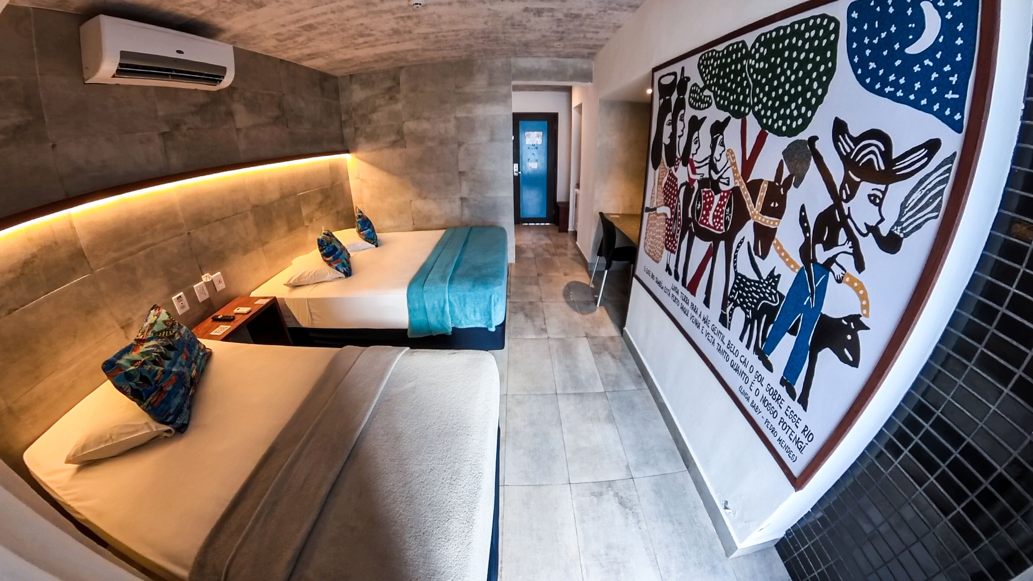 A modern hotel room with a curved bed, a mural, and a hallway leading to a door.