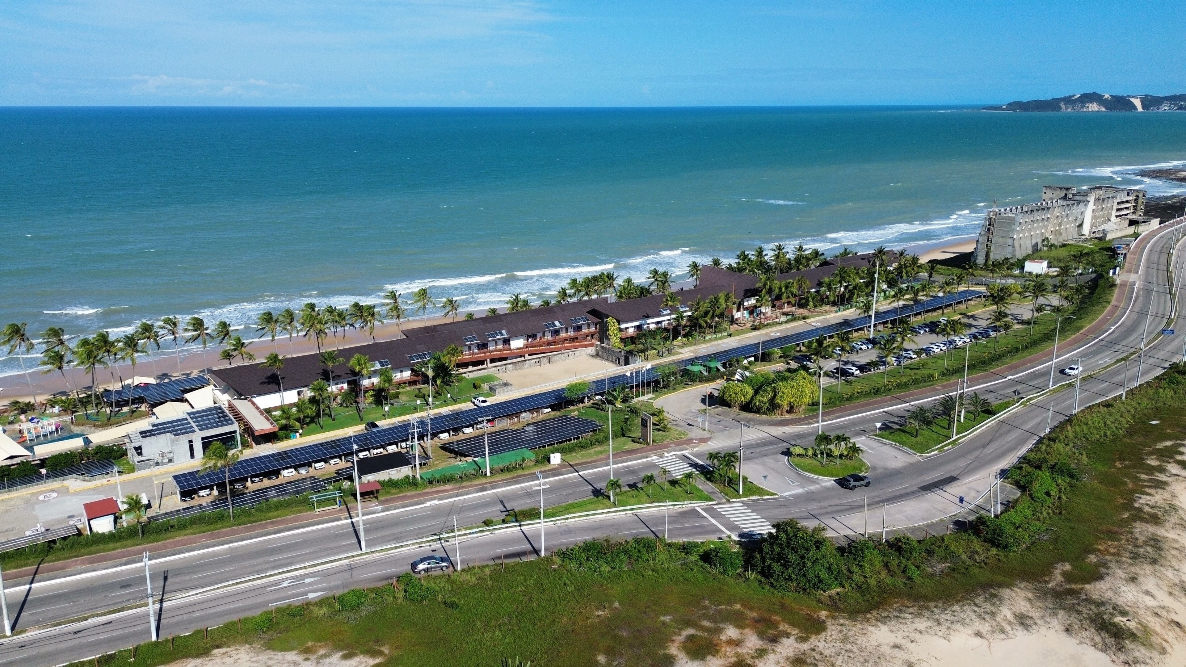 Una strada costiera con una spiaggia su un lato, pannelli solari e un'autostrada.