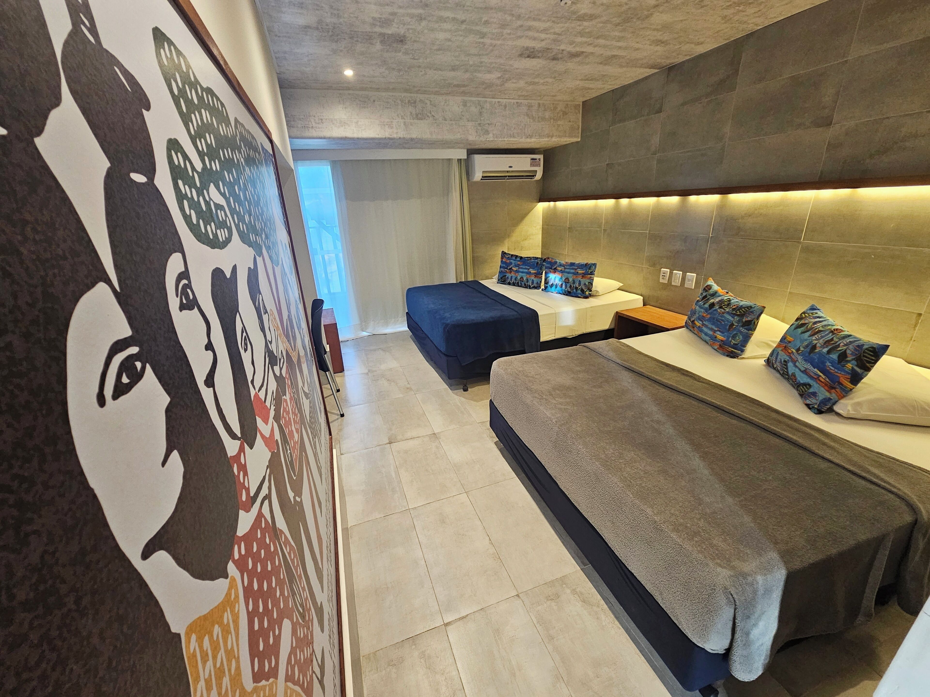A modern hotel room with a large bed, a sofa, a desk, and a mural on the wall.