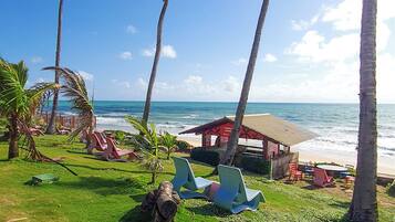 A beachside resort with palm trees, lounge chairs, and a small building with a red roof.