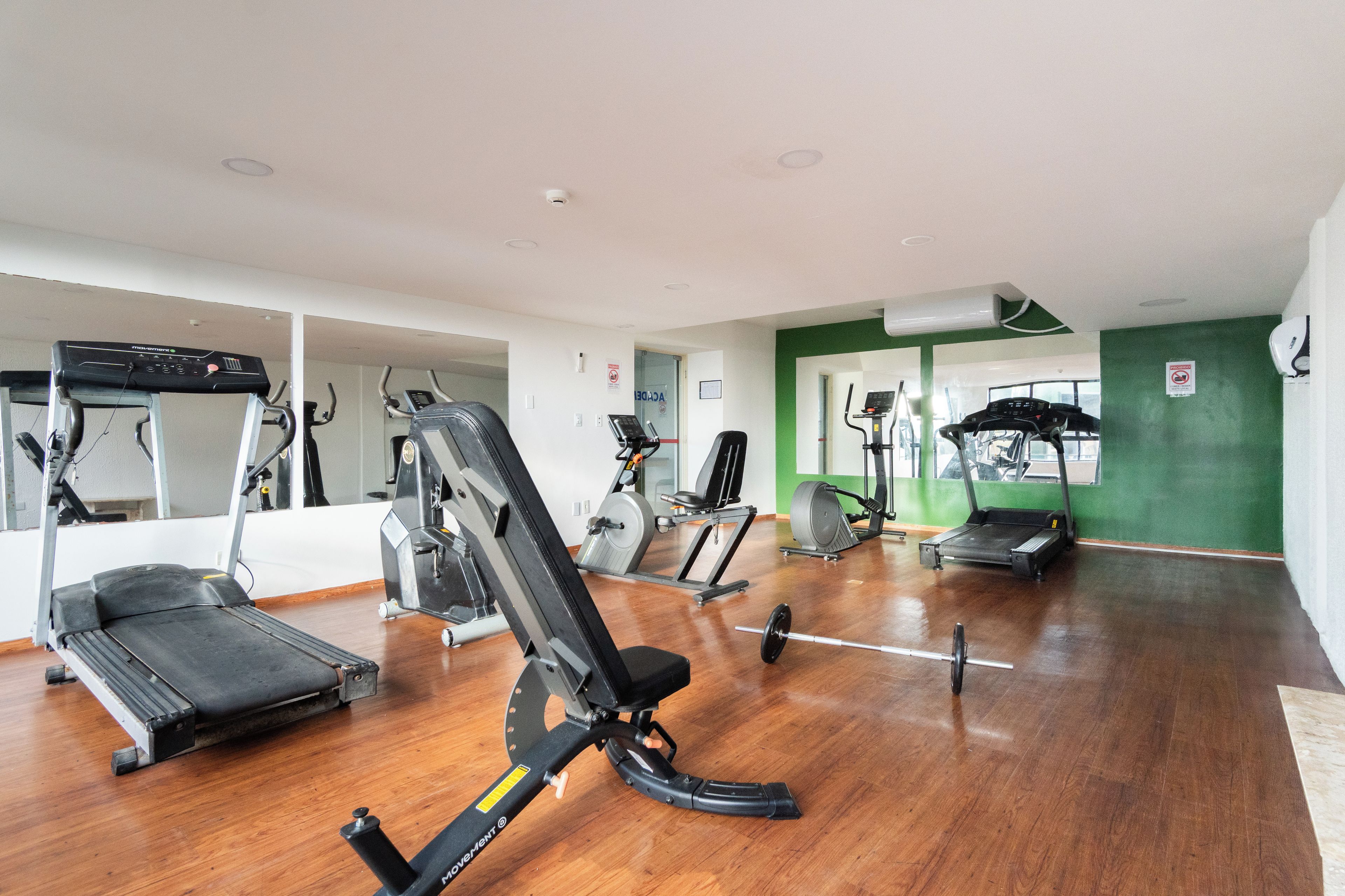 Un gimnasio con diversos equipos de ejercicio, incluyendo cintas de correr, un banco de pesas y una máquina de remo.