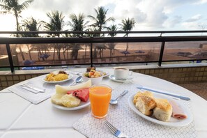 A table with breakfast items including fruit, bread, and a beverage, with a view of palm trees and a beach in the background. - Hotel Dan Inn Mar Piedade - Grande Recife By Nacional Inn (Jaboatão dos Guararapes)