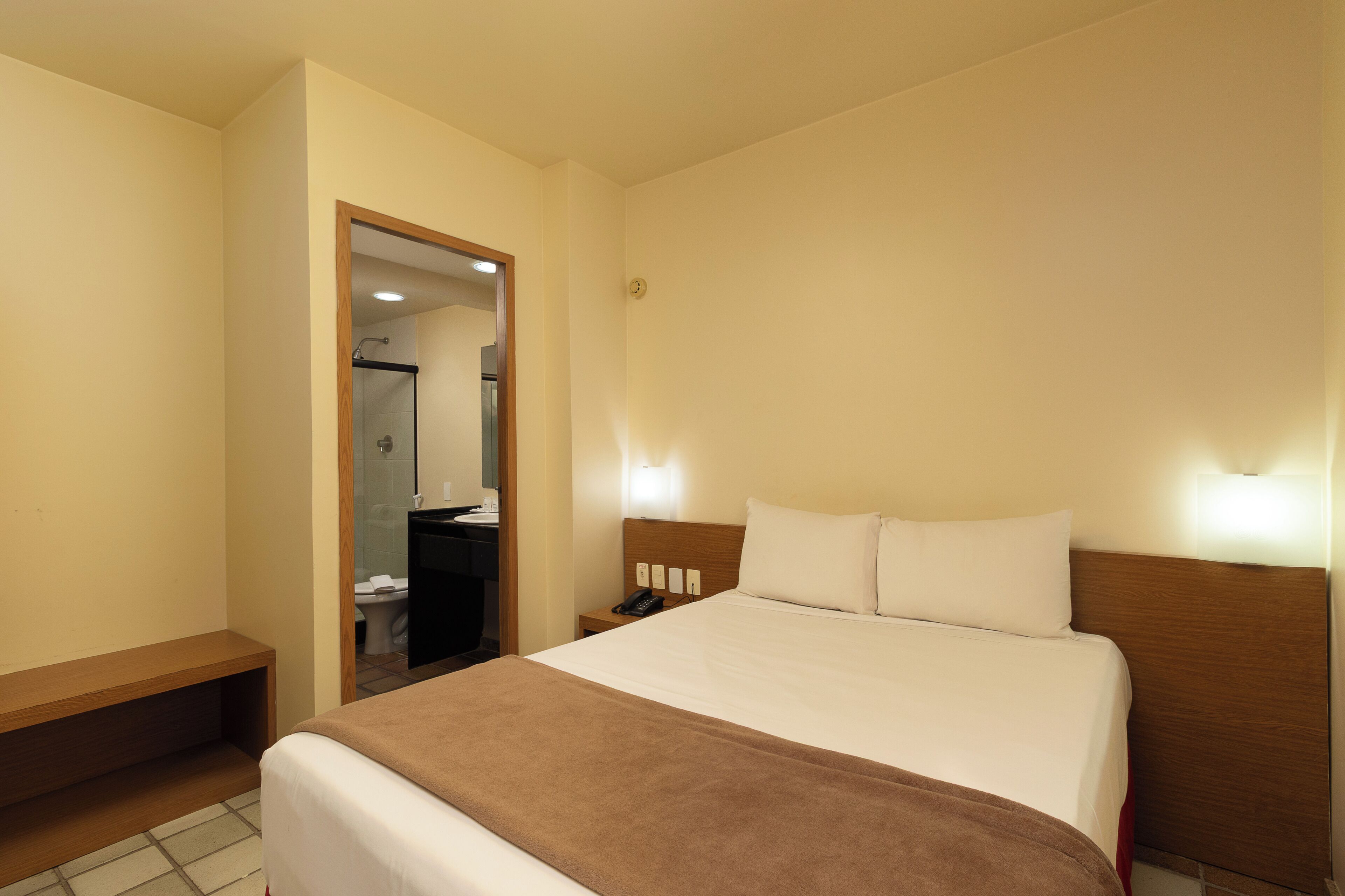 A hotel room with a bed, bedside table, and a bathroom visible through an open door.
