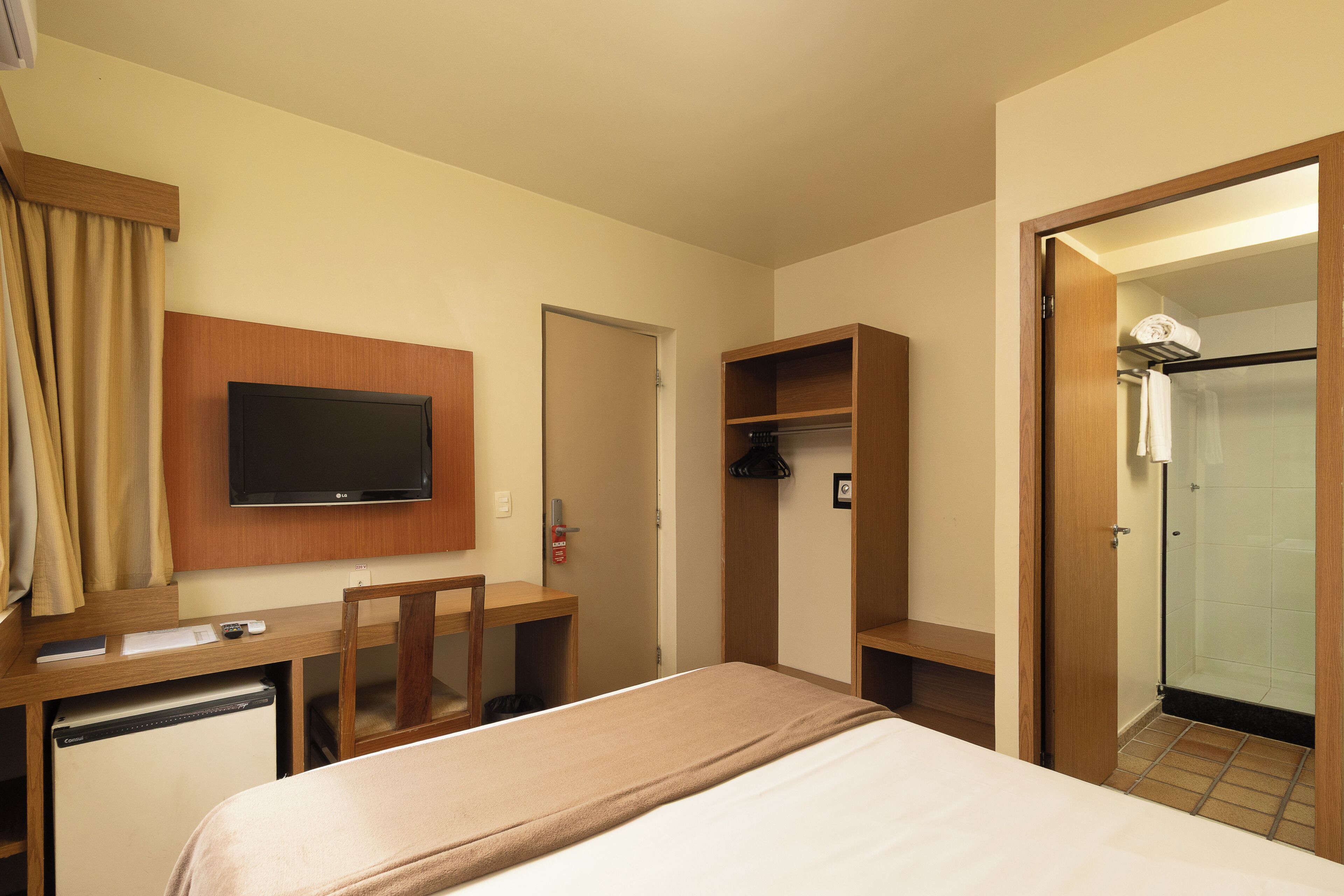 Ein Hotelzimmer mit Bett, Fernseher, Schreibtisch mit Stuhl, Kleiderschrank und Duschbereich.