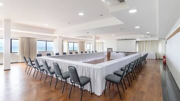 Un salón de conferencias con una larga mesa, sillas y ventanas amplias.