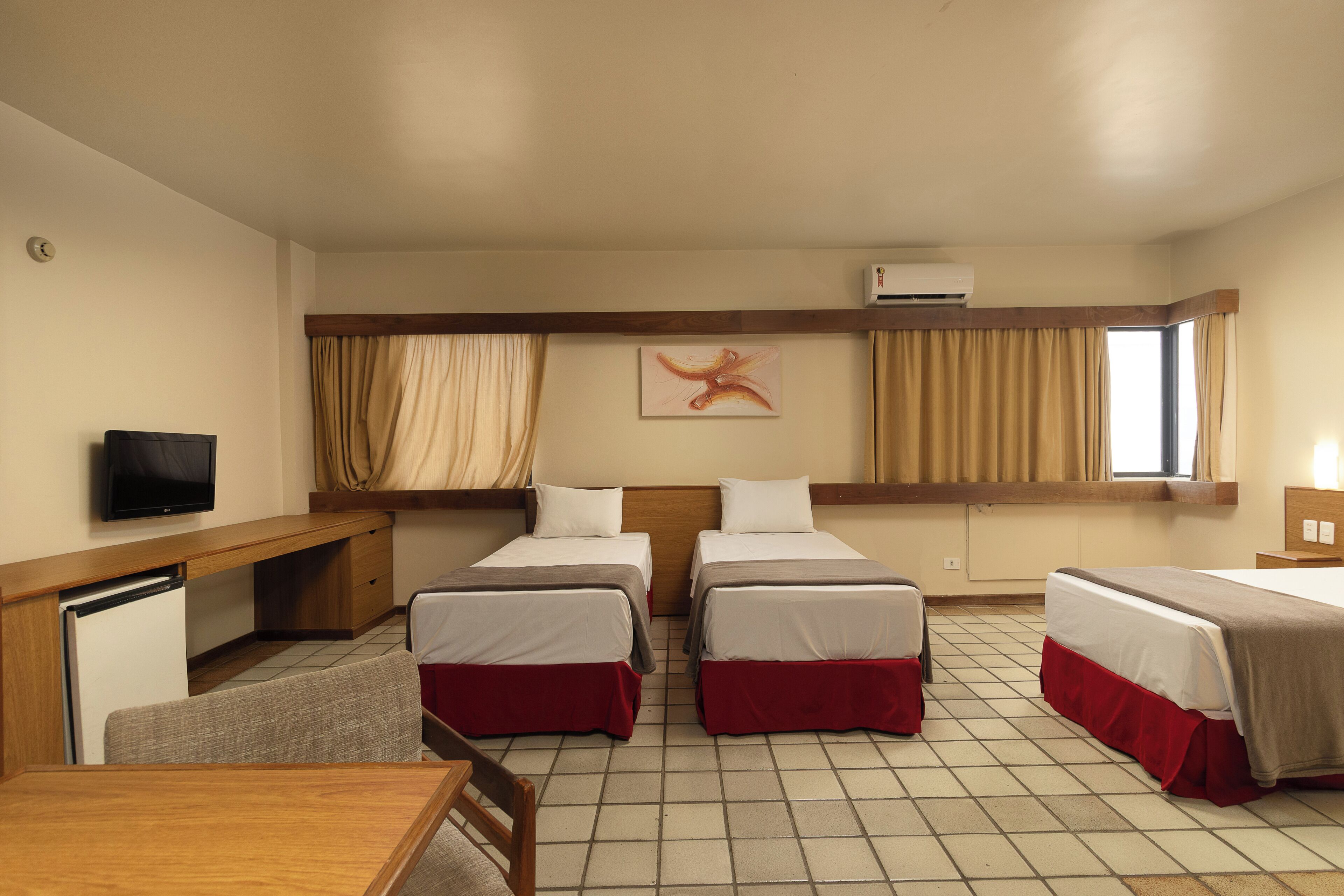 A hotel room with two beds, a desk, a television, and an air conditioning unit.