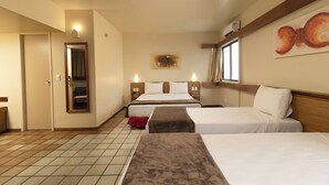 A hotel room with three beds, a mirror, a painting on the wall, and a ceiling fan.