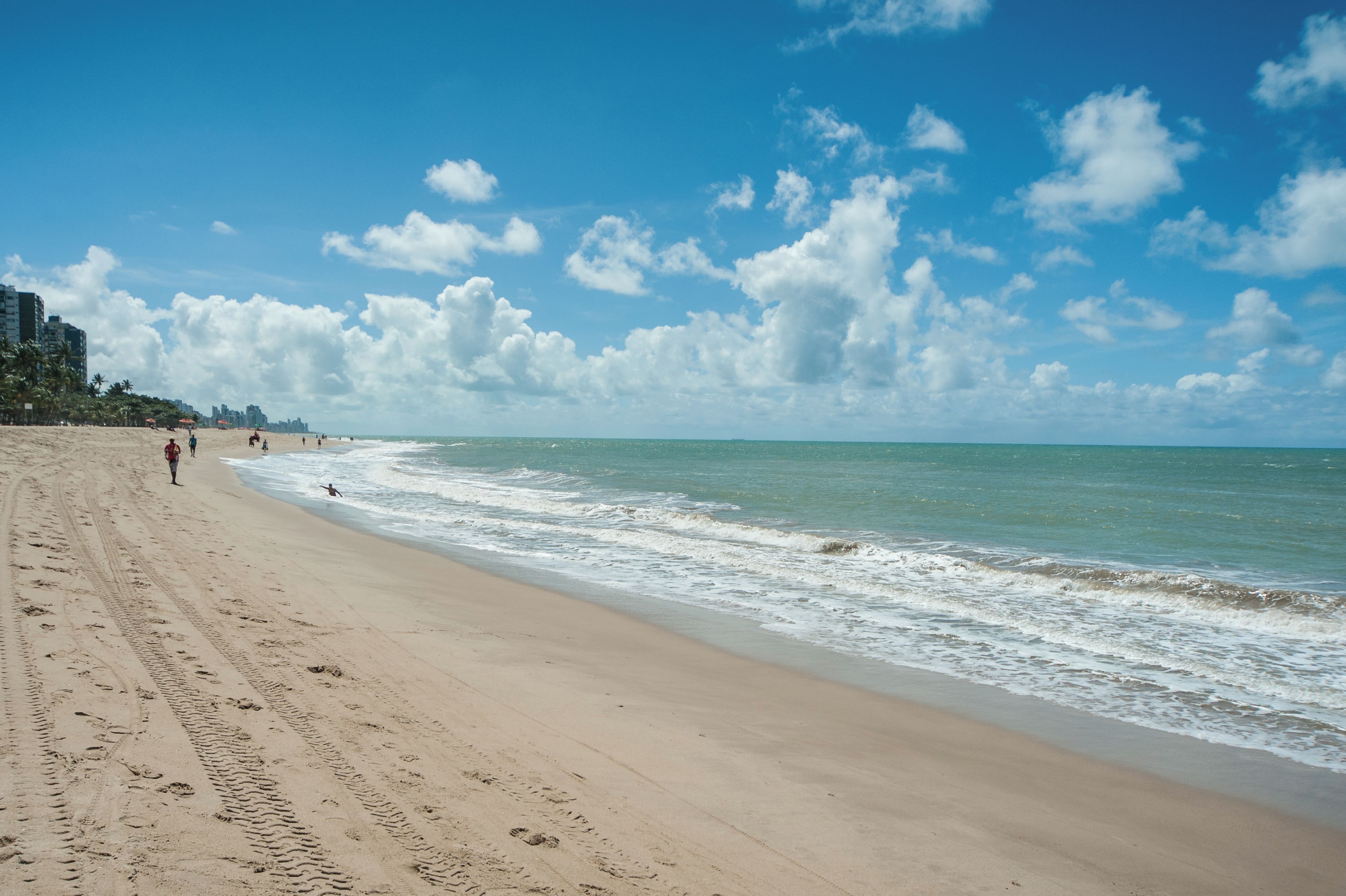 A beach with a sandy shore, ocean waves, and a clear sky with clouds.