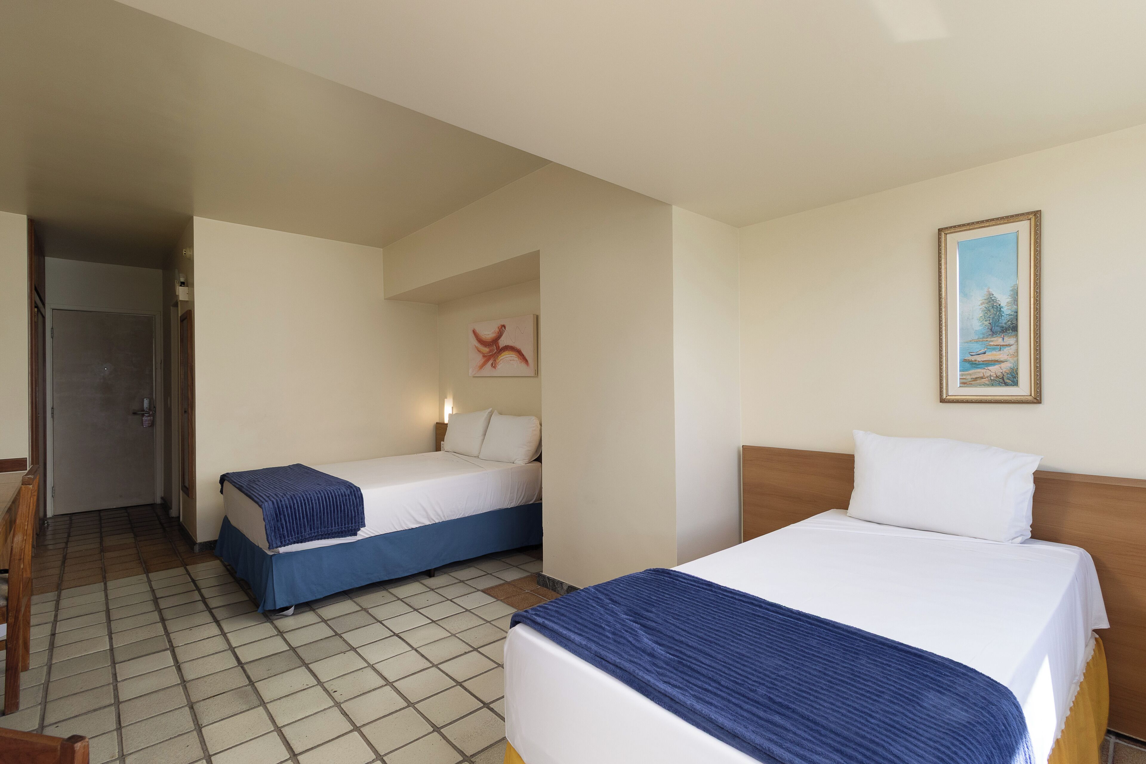 Habitación de hotel con dos camas, un cuadro y piso de baldosas.