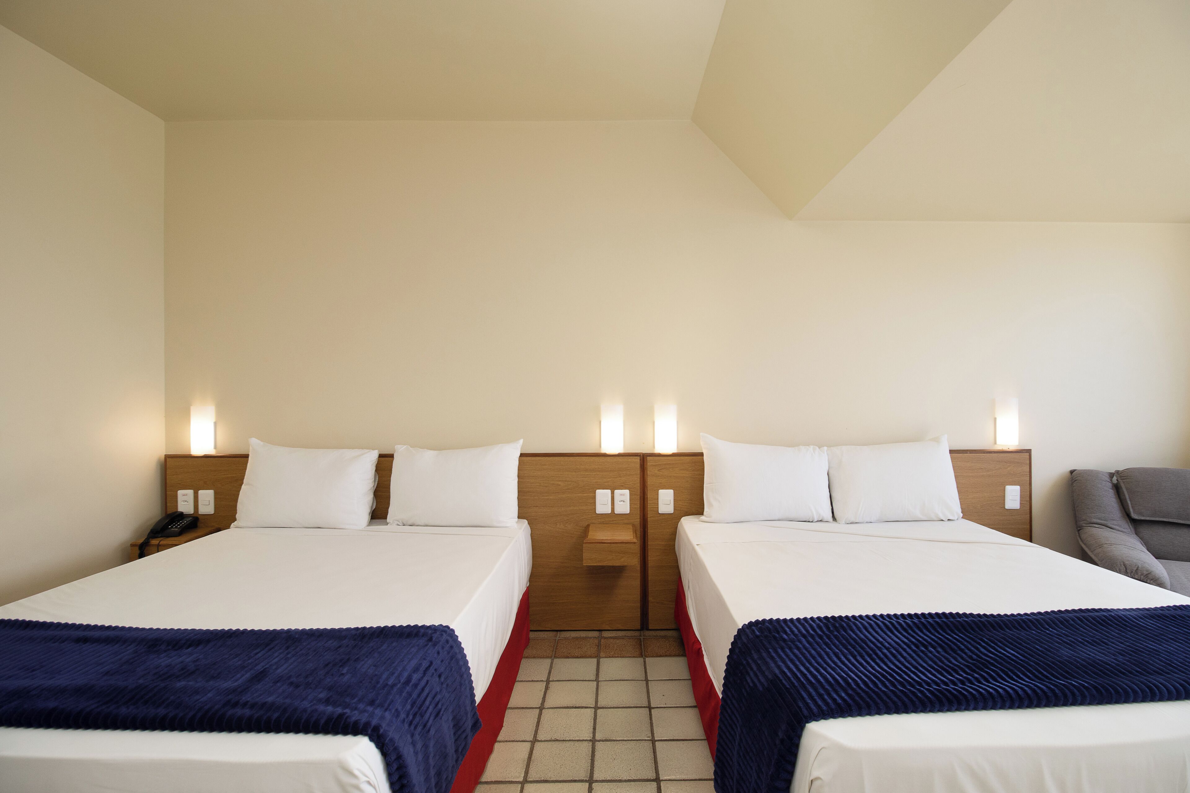 A hotel room with two beds, a nightstand with a phone, and a chair.