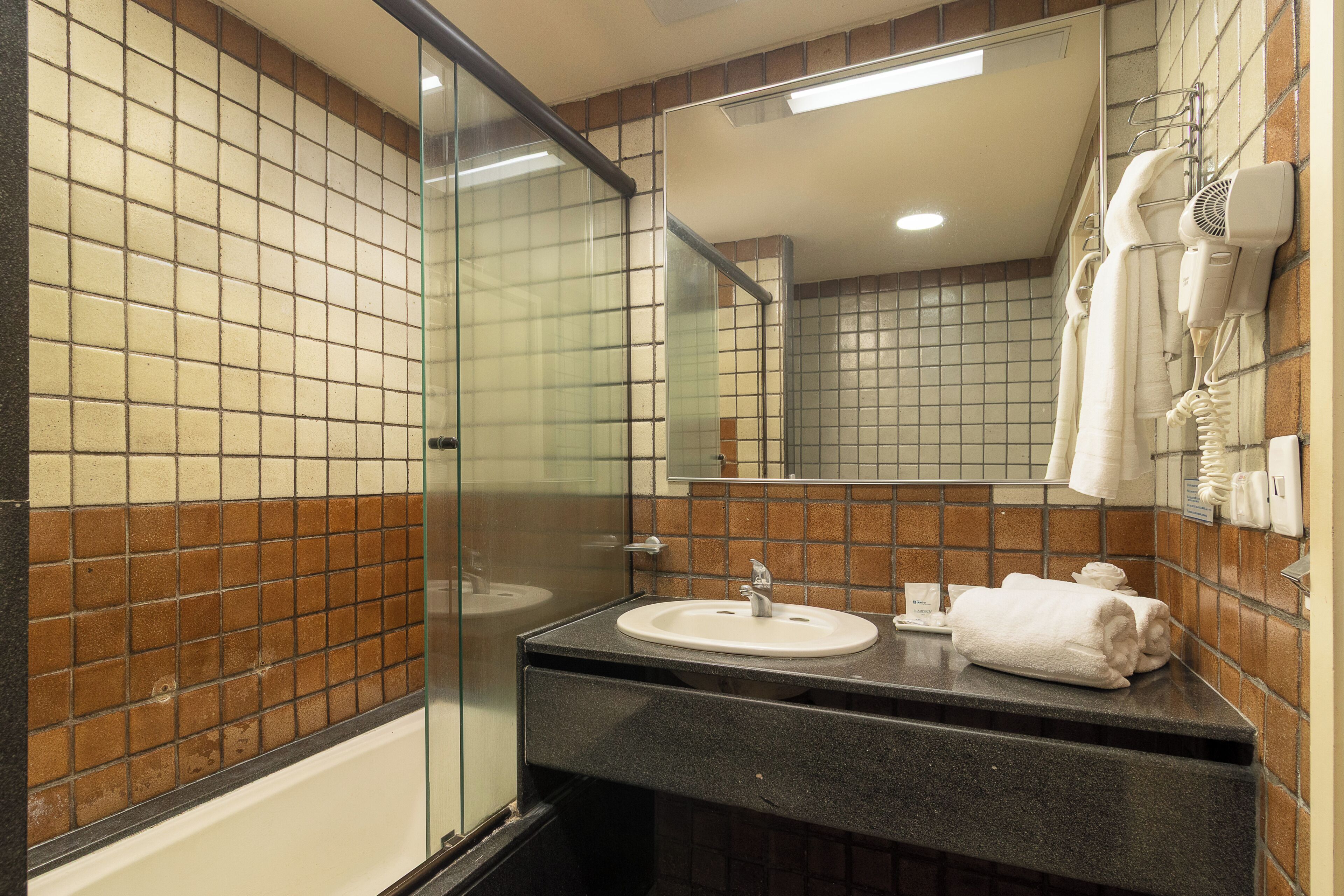 Une salle de bain avec une douche à parois de verre, un lavabo avec un miroir au-dessus et un porte-serviettes avec des serviettes.