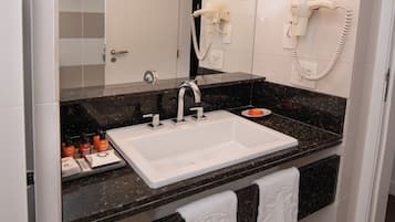 A modern bathroom with a white sink, black granite countertop, and a large mirror. There are two towels hanging on the wall and a white cabinet above the sink.