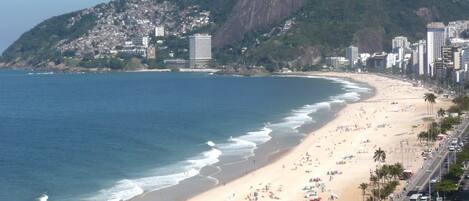 Una playa con una carretera que la bordea, una montaña al fondo y edificios en la ladera.