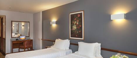Habitación de hotel con dos camas, un escritorio, una silla, un espejo y un cuadro en la pared.