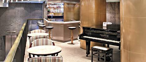Un espace bar avec un piano, des chaises à rayures et un comptoir où sont exposées des bouteilles et des verres.