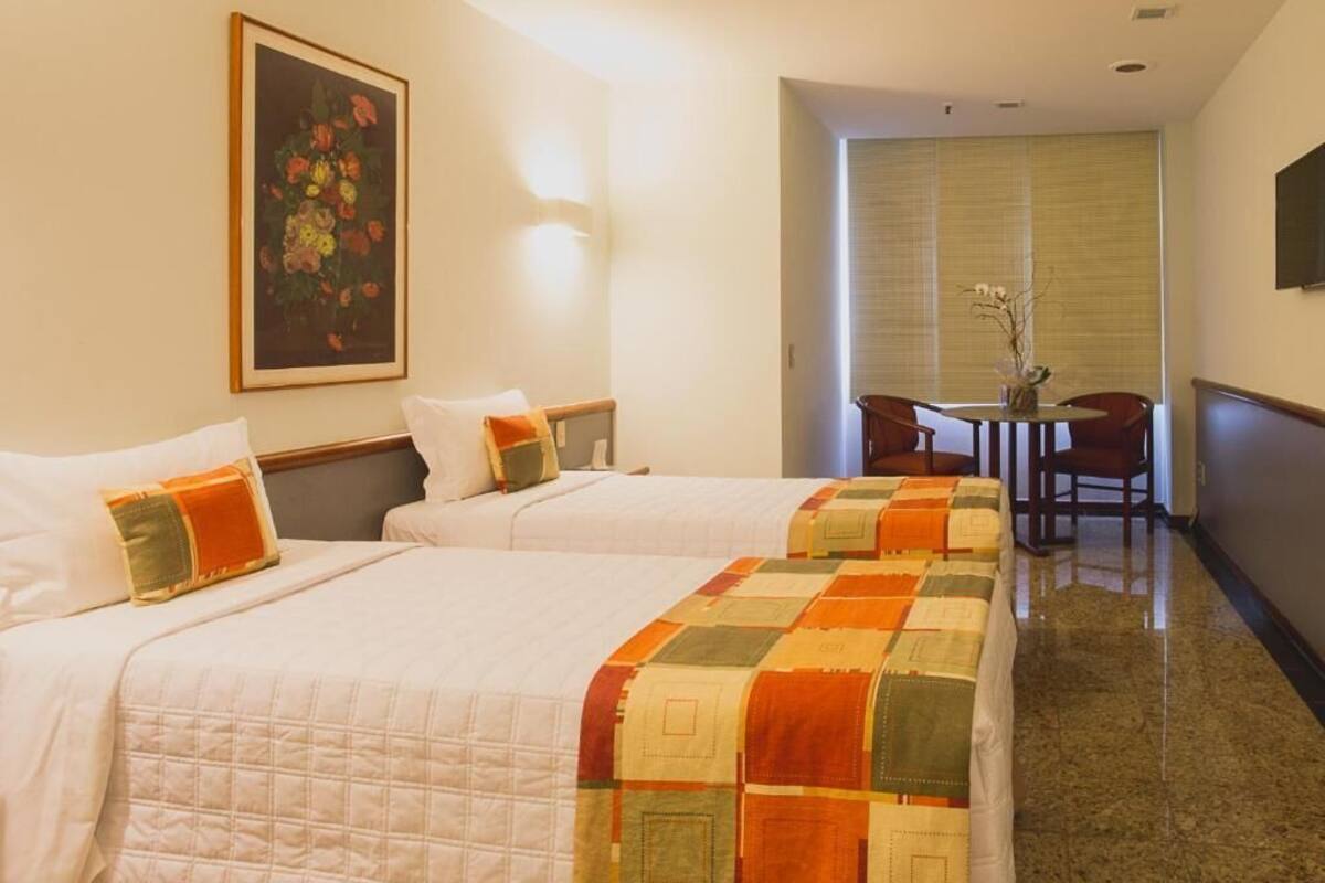 A hotel room with two beds, a dining table with chairs, and a painting on the wall.
