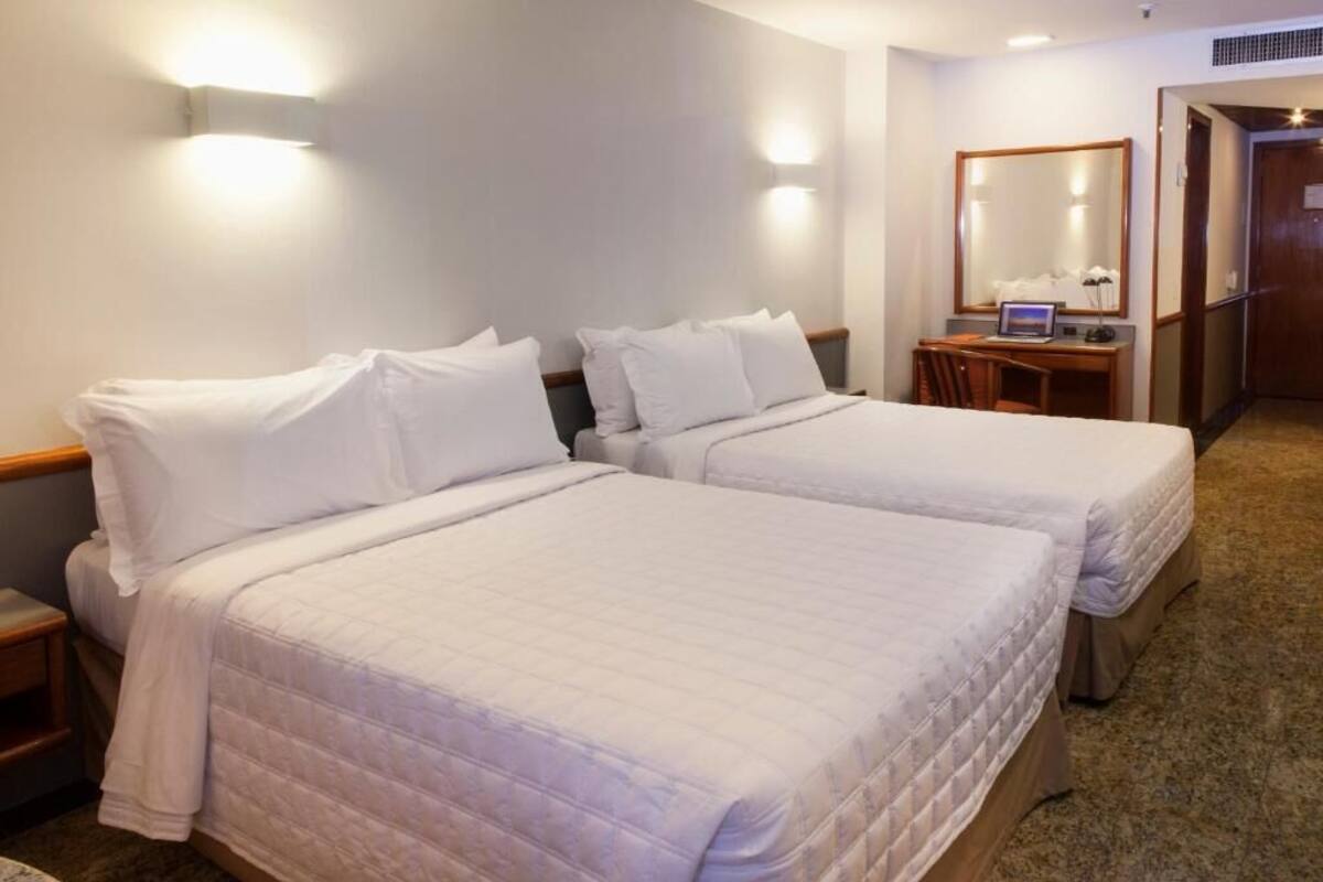 A hotel room with two beds, a desk with a laptop, and a mirror.