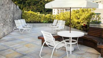 An outdoor patio with white metal chairs and a round table, surrounded by a stone wall and lush greenery.