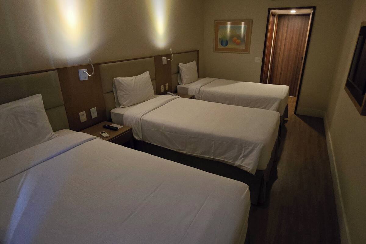 Une chambre d’hôtel avec trois lits simples, une table de chevet avec un téléphone et un tableau au mur.