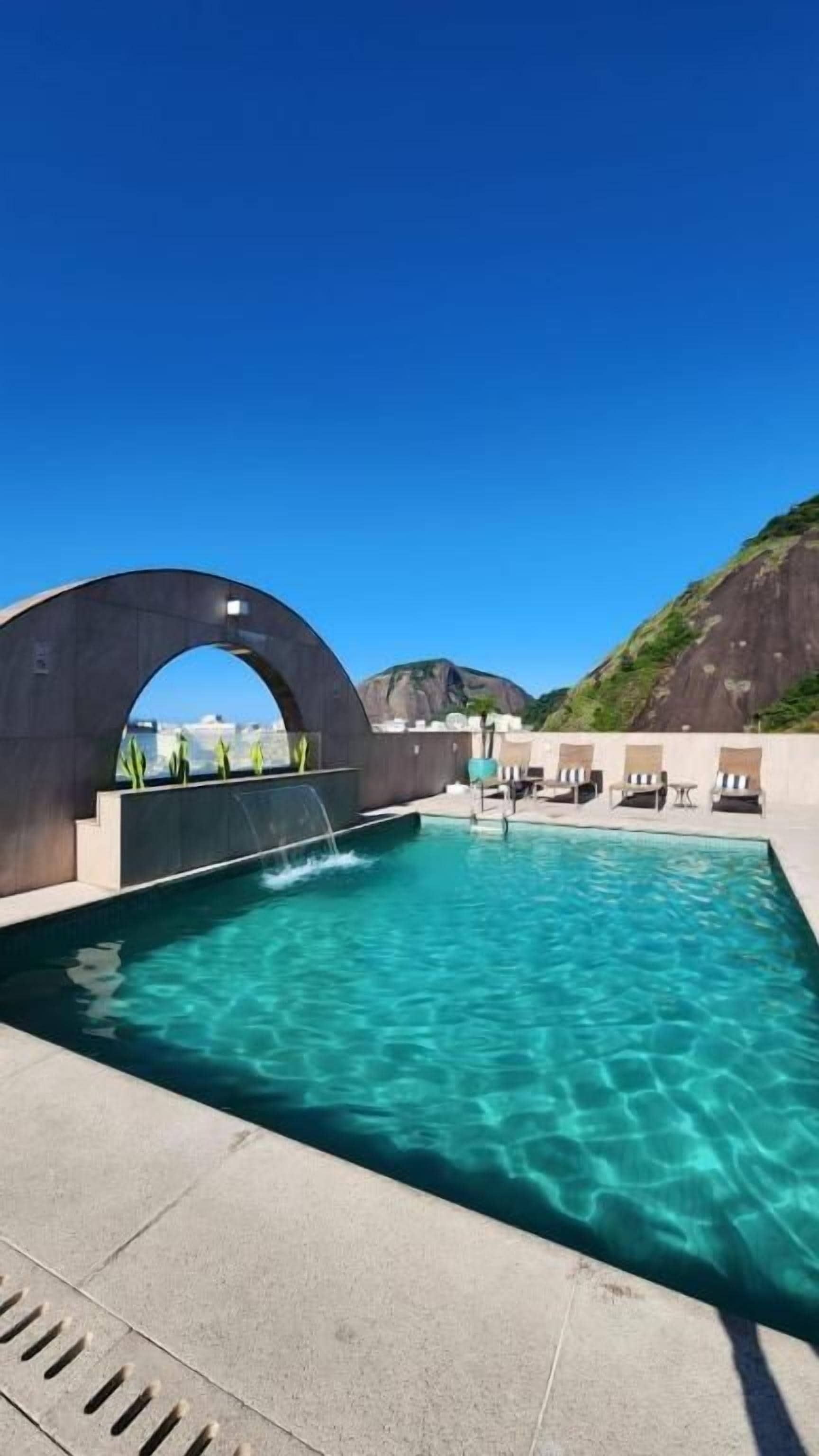 A swimming pool with a clear blue water, a large arched structure, and lounge chairs.