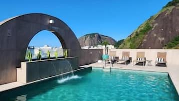 A swimming pool with a clear blue water, a large arched structure, and lounge chairs.