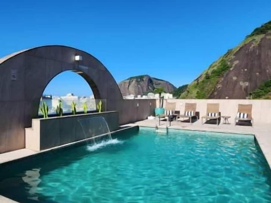 Una piscina con agua cristalina azul, una gran estructura arqueada y sillones de descanso.