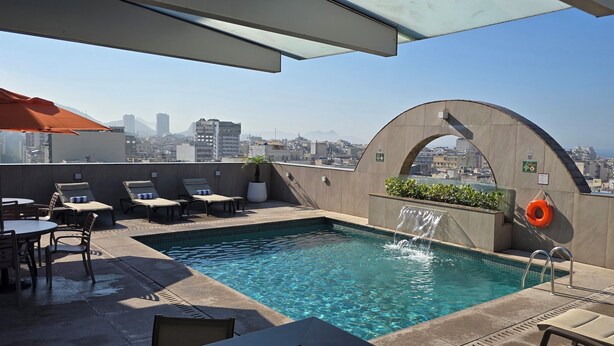 A rooftop pool with a city view, lounge chairs, and a small waterfall feature. - Mirador Rio Hotel (Rio de Janeiro)
