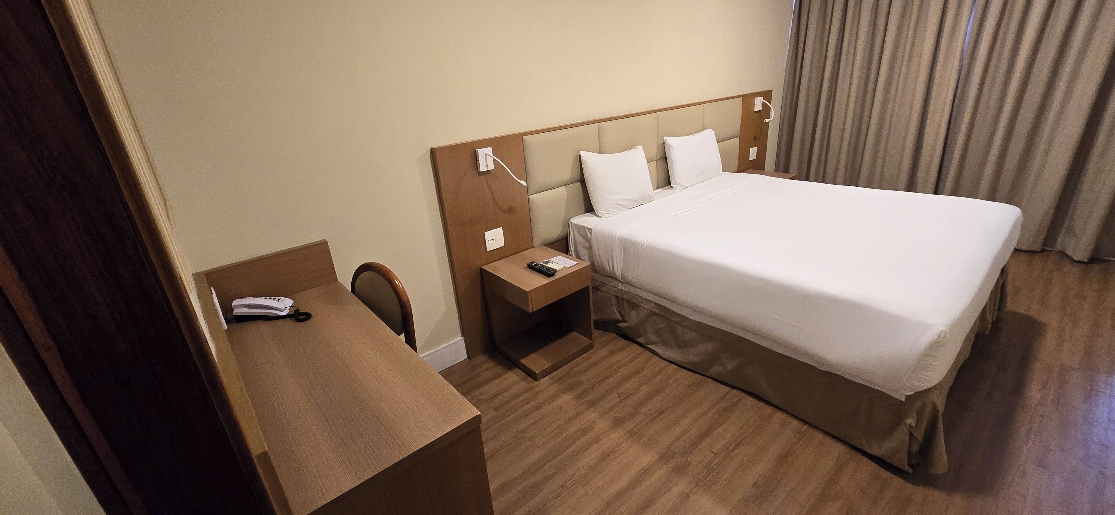 Una habitación de hotel con cama, escritorio, silla, mesita de noche y lámpara.