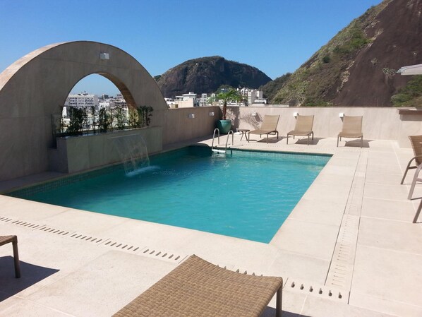 Una piscina al aire libre, sombrillas, sillones reclinables de piscina