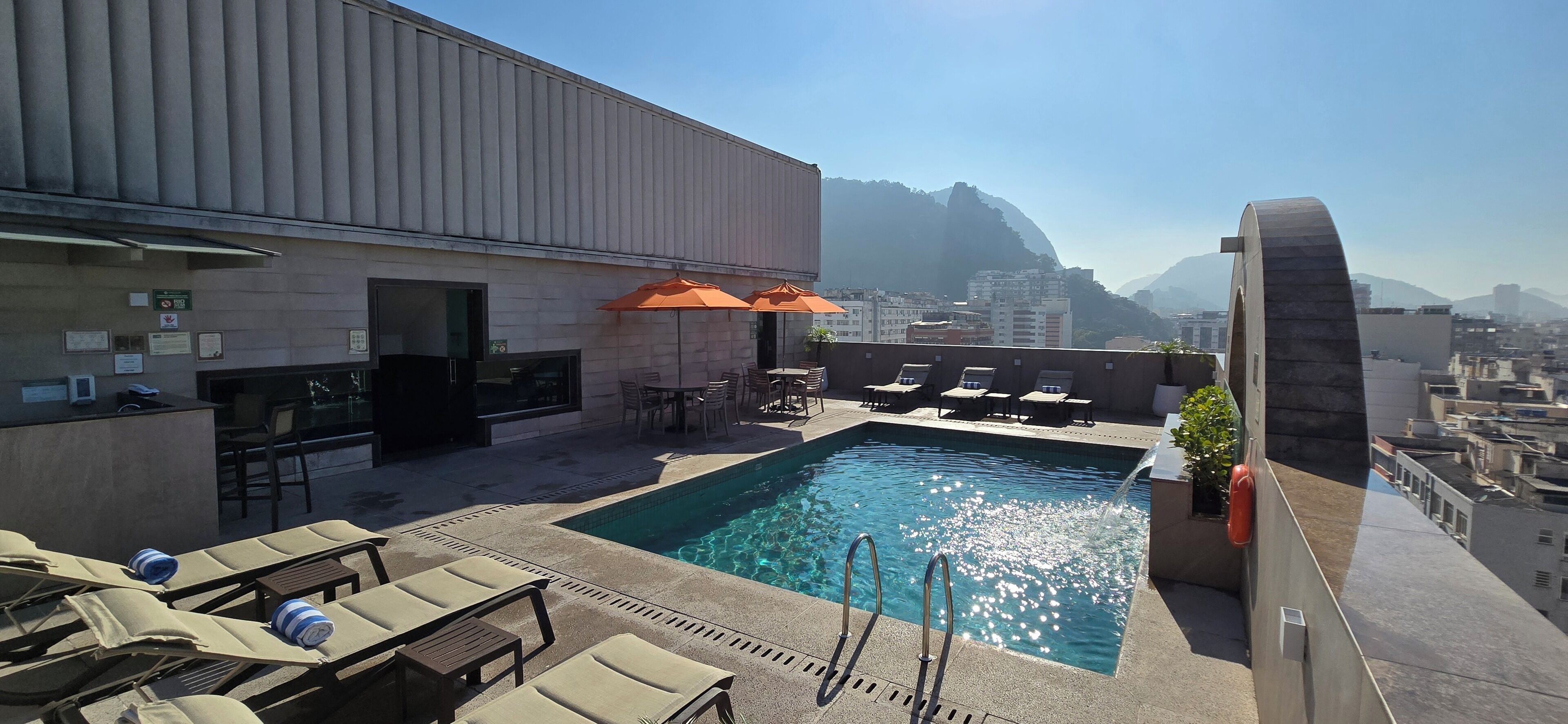Ein Poolbereich auf dem Dach mit Liegestühlen, einem Pool und Blick auf Stadt und Berge.
