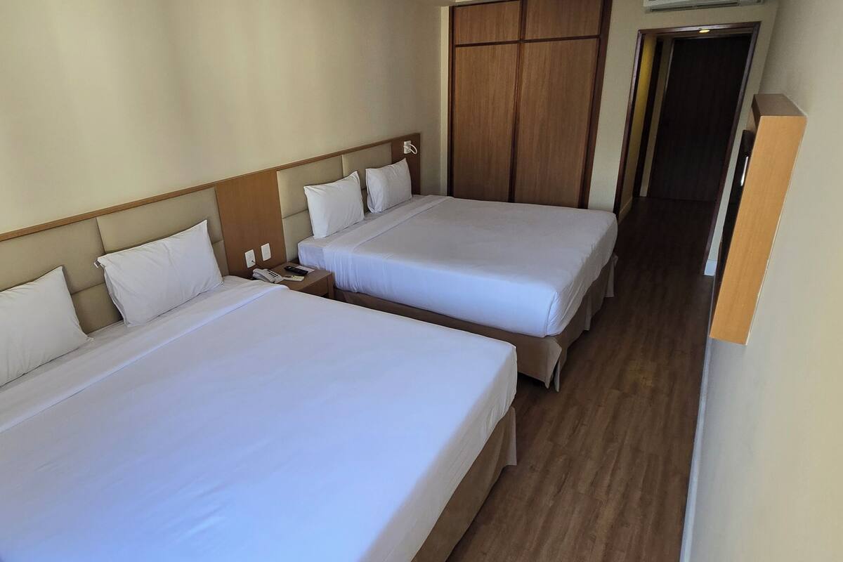 Une chambre d’hôtel avec deux lits simples, des têtes de lit en bois, une armoire et une petite table de chevet avec un téléphone.