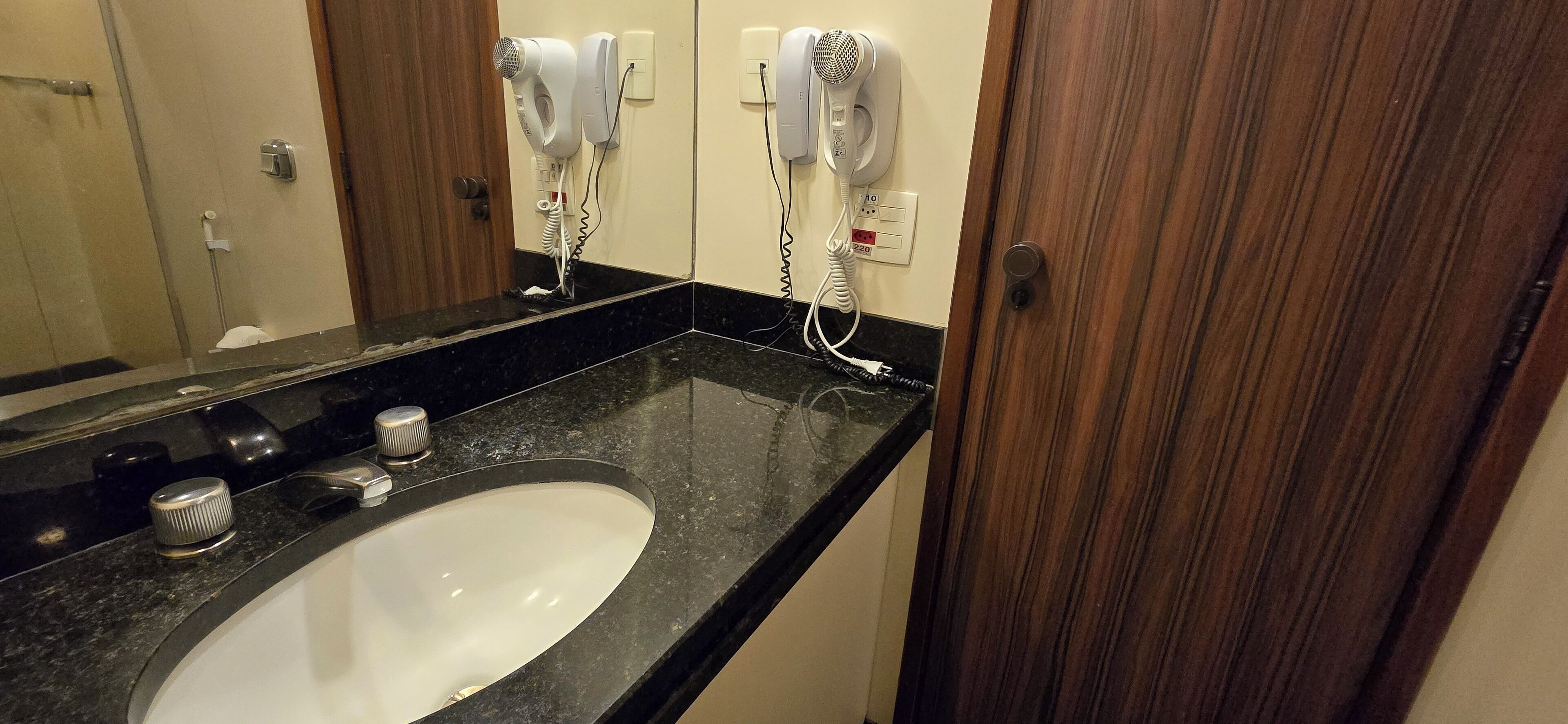 A bathroom with a black countertop, a white sink, and two hair dryers mounted on the wall.