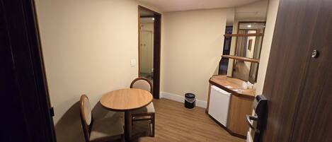 Una cocina pequeña y funcional con una mesa y sillas de madera, un refrigerador y un bote de basura.