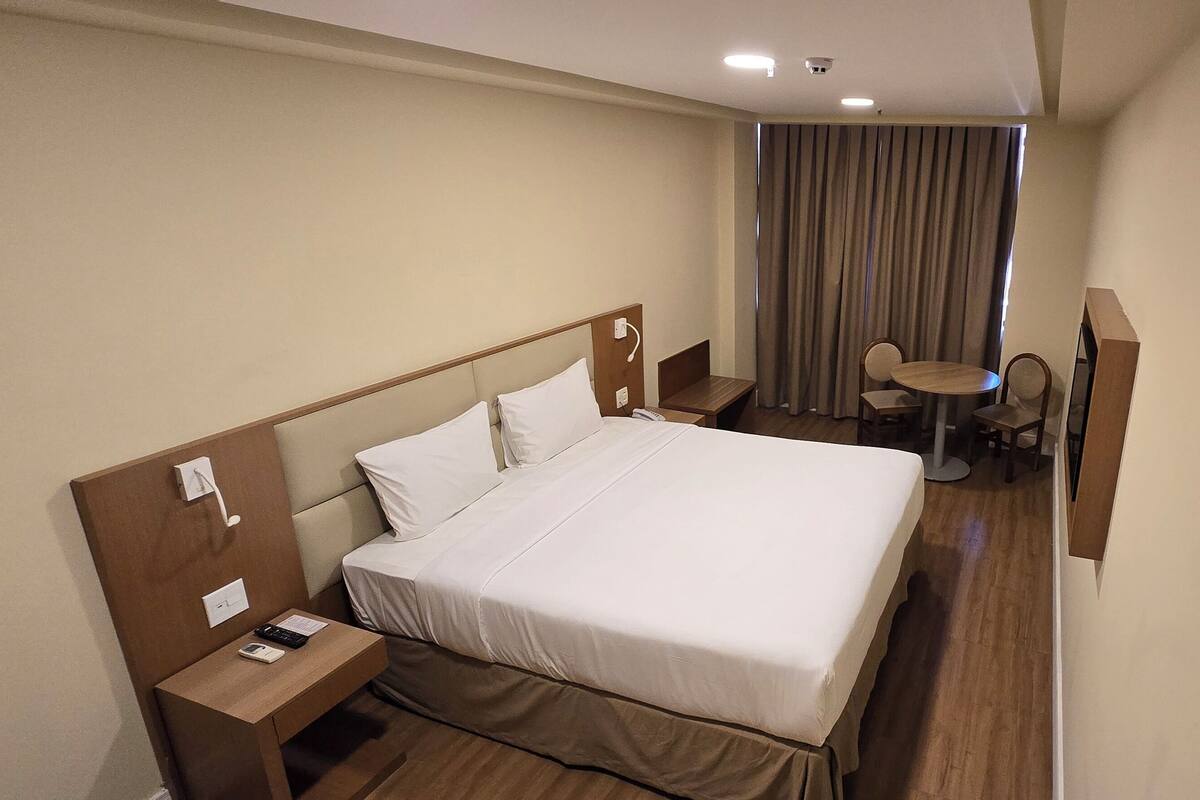 Une chambre d’hôtel avec un grand lit, une table de chevet avec un téléphone et un chargeur, une petite table avec des chaises et un téléviseur.
