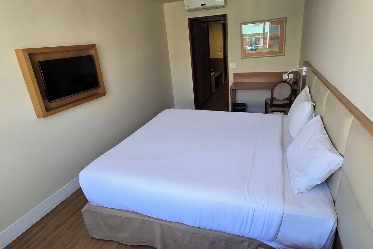 Une chambre d’hôtel avec un lit, un bureau, une chaise, une télévision et une fenêtre.