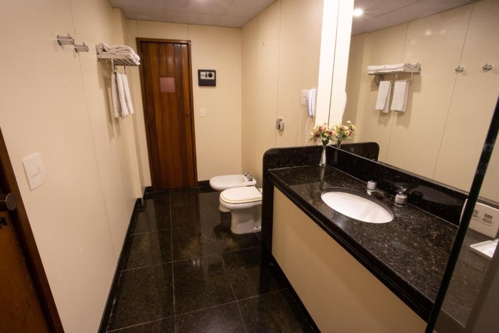 A bathroom with a black marble countertop, a white sink, two toilets, and a wooden door.