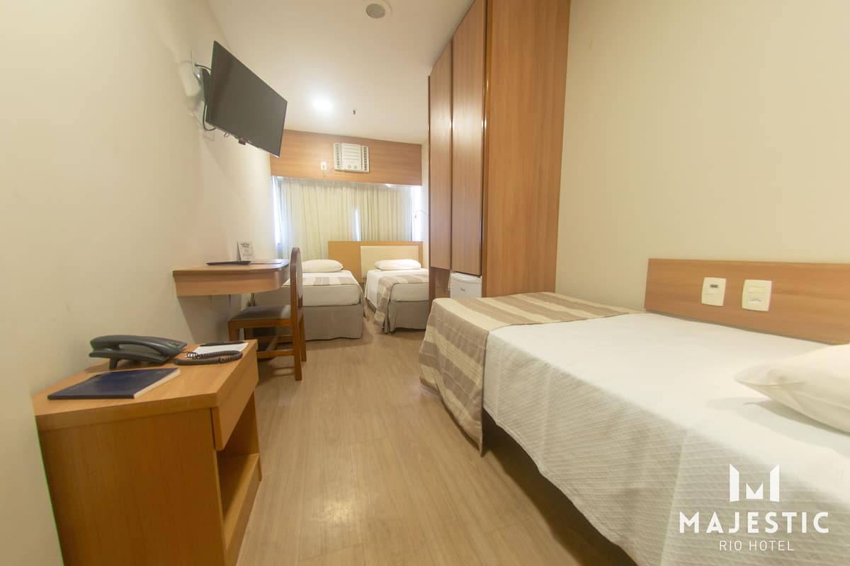 A hotel room with a bed, a desk with a phone, a chair, and a television mounted on the wall.