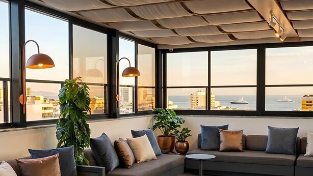 A modern lounge area with a sofa, round tables, potted plants, and large windows offering a city view. - Majestic Rio Palace Hotel (Rio de Janeiro)