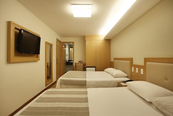 Habitación de hotel con dos camas, un televisor montado en la pared y una pequeña zona de kitchenette.