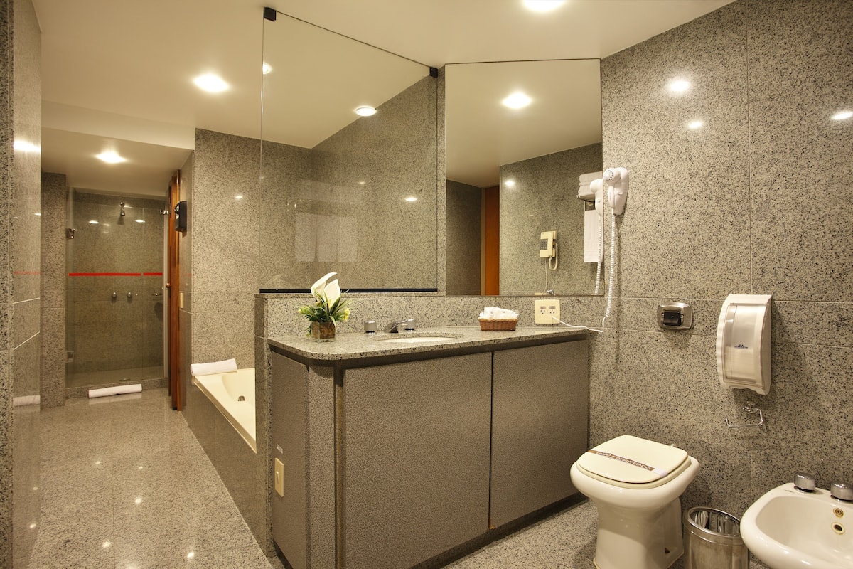 A modern bathroom with a granite countertop, a white toilet, a sink, and a shower area.