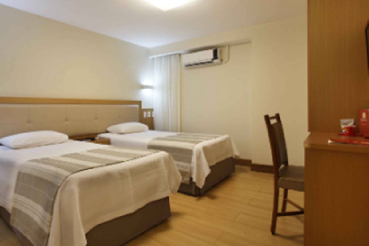 A hotel room with two beds, a chair, a desk, and an air conditioning unit.