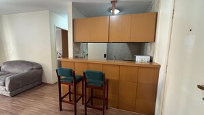 A compact living space with a kitchenette, a grey sofa, and two bar stools. - London Class Hotels (São Paulo)