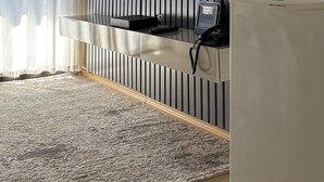 A modern living room with a flat-screen TV mounted on a wall with vertical lines, a built-in kitchen counter with a refrigerator, and a large area rug on the floor. - London Class Hotels (São Paulo)