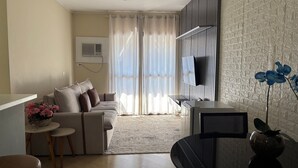 A living room with a sofa, a small table with flowers, a TV, and a decorative plant. - London Class Hotels (São Paulo)