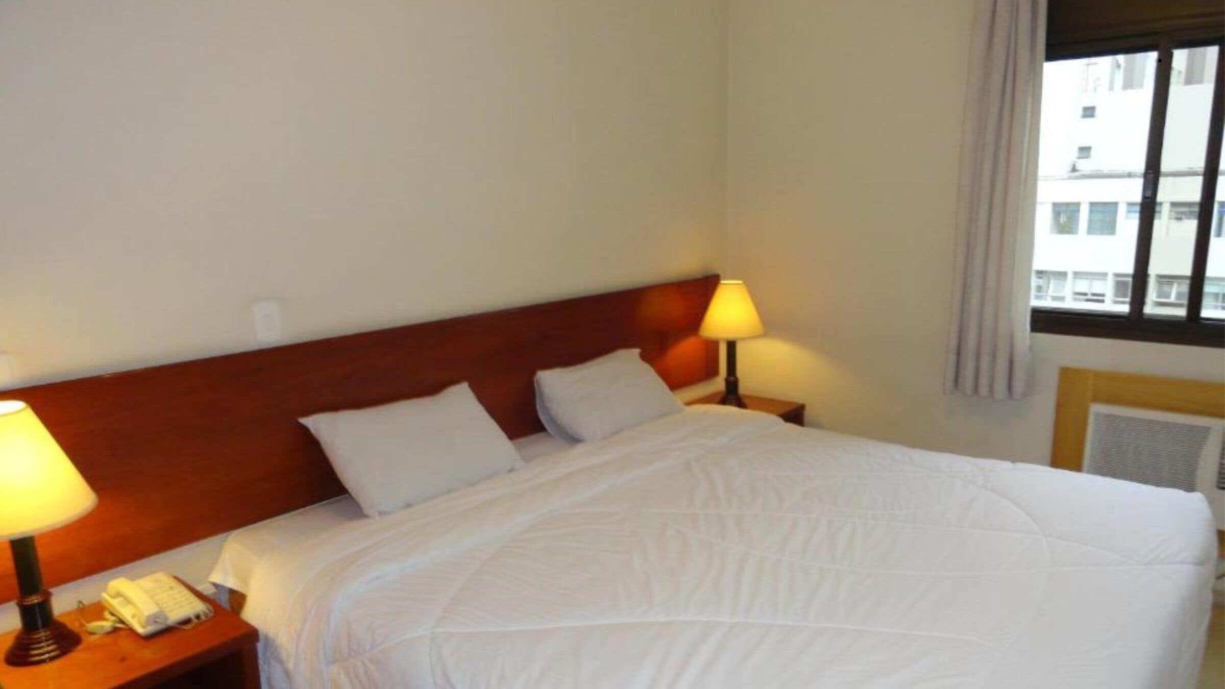 A hotel room with a large bed, two bedside lamps, a telephone, and a window with curtains.