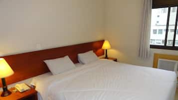 Quarto de hotel com uma cama grande, duas luminárias de cabeceira, um telefone e uma janela com cortinas.
