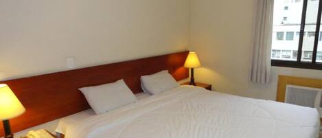 Ein Hotelzimmer mit einem großen Bett, zwei Nachttischlampen, einem Telefon und einem Fenster mit Vorhängen.